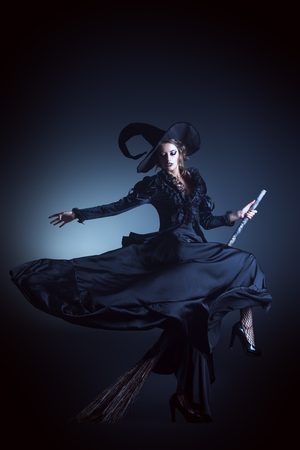 Portrait of a gorgeous brunette witch flying on a broom over black background. Halloween.の写真素材