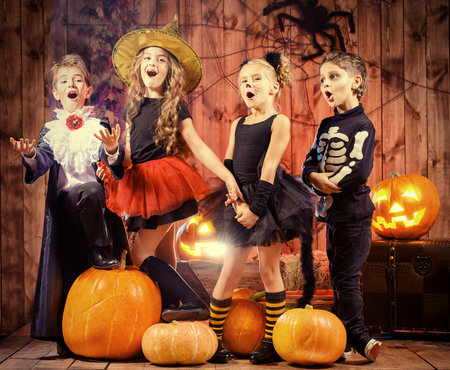 Cheerful children in halloween costumes celebrating halloween in a wooden barn with pumpkins.の写真素材