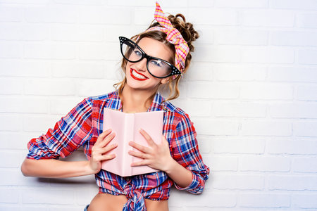 Funny glamorous pin-up girl in elegant huge glasses reading a book.の写真素材