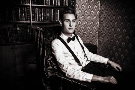 Elegant handsome young man sitting by the fireplace in a room with classic vintage interior. Fashion shot.の写真素材