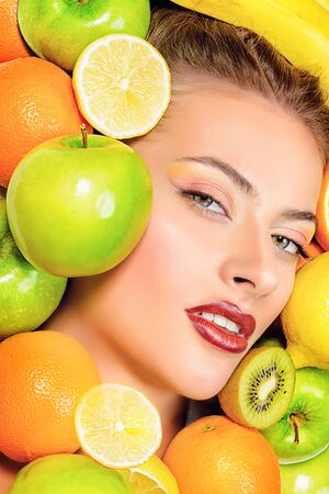 Close-up portrait of a beautiful smiling woman among fresh fruits.の写真素材