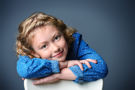 Pretty smiling eight-year girl in jeans dress posing at studio.の写真素材