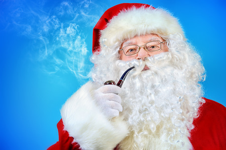Portrait of a traditional Santa Claus smoking a pipe. Blue background.の写真素材