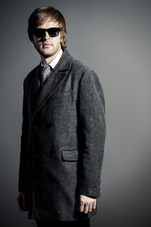 Elegant young man in a coat and sunglasses.の写真素材