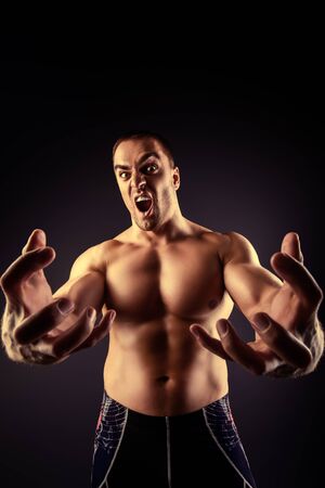 Muscular bodybuilder man stretching his arms to the camera and shouting over black background.の写真素材