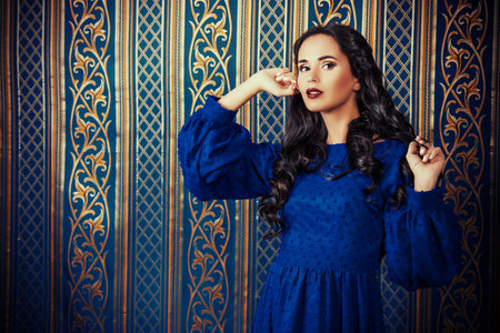 Beautiful pregnant woman in elegant evening dress posing over vintage background. Fashion shot.