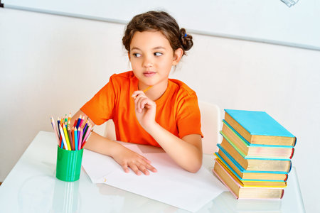 Pretty smart schoolgirl sitting at the desk in the classroom on blackboard background. Education.