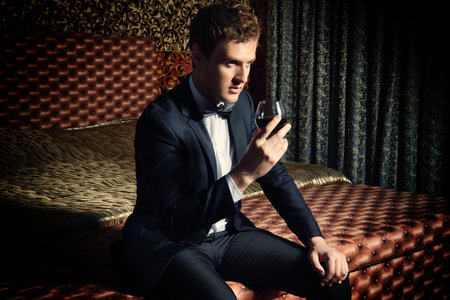 Imposing young man in elegant suit with glass of beverage. Luxury. Vintage interior. Fashion shot.