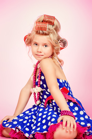 Beautiful little girl in her mother's hair curlers and polka-dot dress. Kid's fashion, cosmetics. Pin-up style.の写真素材