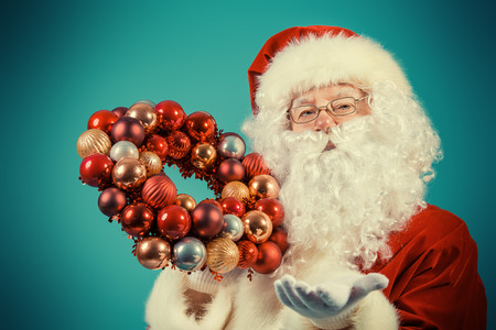 Portrait of a traditional Santa Claus holding Christmas wreath over blue background. Studio shot. Christmas.の写真素材
