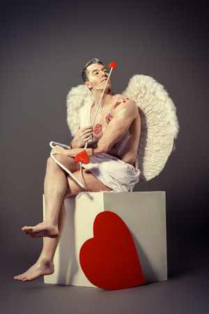 Tired angel Cupid with a bow and arrows of love having a rest with a cup of tea. Valentine's day. Love concept.の写真素材