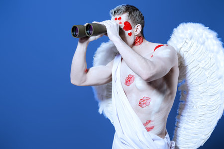 Handsome male angel Cupid looking for something with binoculars. Valentine's day. Love concept.