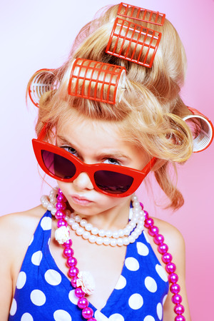 Fashionable little girl in her mother's hair curlers and pin-up sunglasses. Kid's fashion, cosmetics. Pin-up style.の写真素材