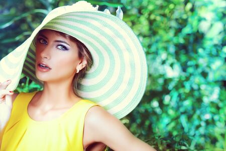 Beautiful romantic woman in light dress and elegant hat posing in a blooming garden. Beauty, fashion.の写真素材
