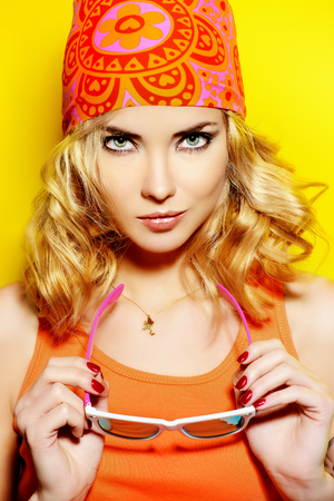 Pretty girl with curly blonde hair wearing bright clothes and sunglasses posing over yellow background. Bright style, fashion.の写真素材