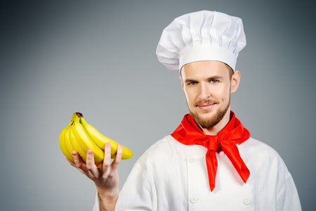 Closeup portrait of a smiling male cook holding bananas. Healthy eating. Copy space. Studio shot.の写真素材