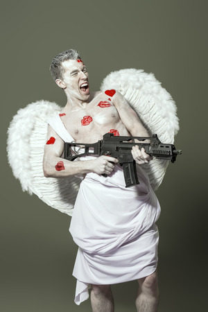 Masculine male angel Cupid with a gun instead of a bow and arrows of love. Valentine's day. Love concept.の写真素材