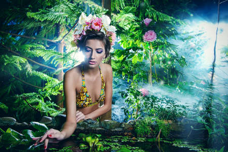 Tender beautiful girl in a flower wreath sits by a pond in the rainforest. Beauty, bodycare. Tropical vacation.の写真素材