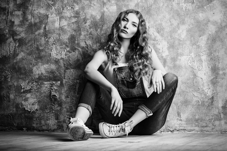 Pretty red-haired girl in casual jeans clothes alluring by a grunge wall. Youth fashion.の写真素材