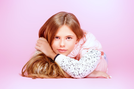 Smiling girl teenager with beautiful healthy long hair lying on a floor over pink background. Studio shot.の写真素材