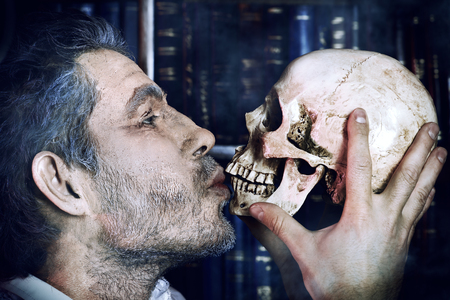 Close-up portrait of an old medieval scientist holding a skull.の写真素材