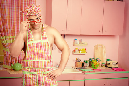 Handsome muscular man in an apron cooking in the pink kitchen. Love concept. Valentine's day.の写真素材