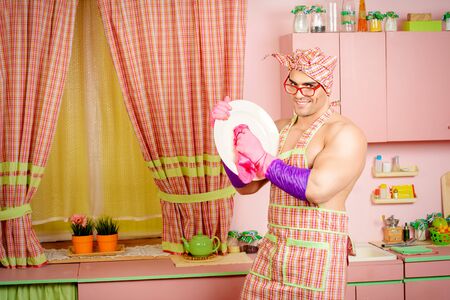 Handsome muscular man in an apron washing the dishes the pink kitchen. Love, family concept. Valentine's day.の写真素材