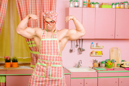 Handsome muscular man in an apron cooking in the pink kitchen. Love concept. Valentine's day.の写真素材