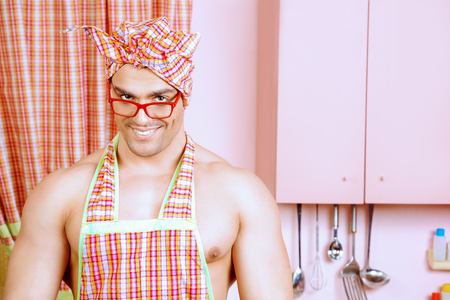 Handsome muscular man in an apron cooking in the pink kitchen. Love concept. Valentine's day.の写真素材