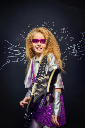 Little rock star singing with her electric guitar over musical background. Music concept.の写真素材