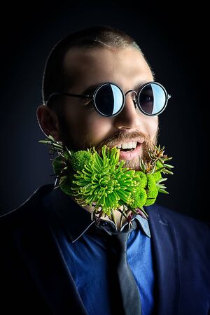 Handsome man in sunglasses and with a beard of green flowers smiling at camera. Men's beauty. Barbershop.の写真素材