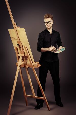 Male artist paints on an easel in the workshop. Occupation.の写真素材