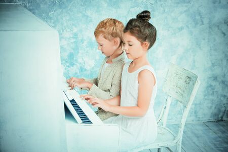 Romantic children playing the white piano. Music and art concept. Vintage, retro style.の写真素材
