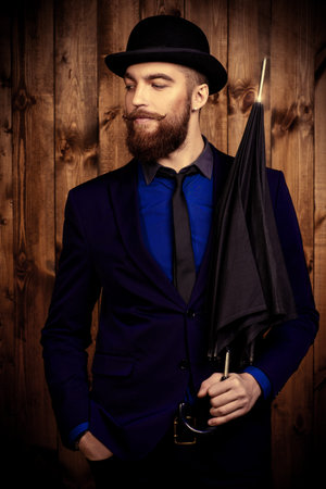 Elegant man with beard and mustache wearing suit and bowler hat. Old style fashion.の写真素材