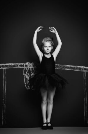 Beautiful girl ballet dancer in black leotard and tutu posing in studio over black background.の写真素材