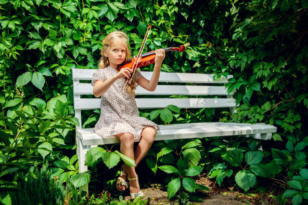 Pretty little girl playing the violin at a summer park.の写真素材