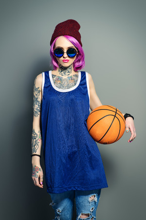 Style of modern youth. Bright girl in sports shirt holding basketball. Tattoo style. Hair coloring.の写真素材