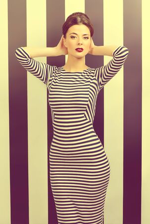 Stylish woman in elegant fitting dress and pin-up hairstyle posing at studio. Beauty, fashion concept.の写真素材