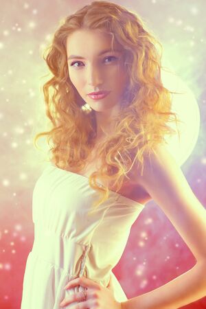 Beautiful romantic girl with wavy hair in light white dress over pink background. Spring look. Natural make-up.の写真素材