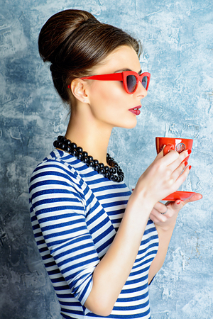 Fashionable lady in elegant dress and pin-up hairstyle posing at studio. Pin-up glasses, optics style. Beauty, fashion concept.の写真素材