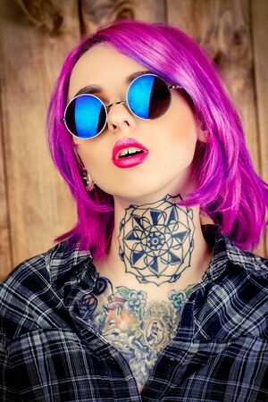 Close-up portrait of a modern girl with bright crimson hair and round sunglasses. Tattoo. Hair coloring. Optics style.の写真素材