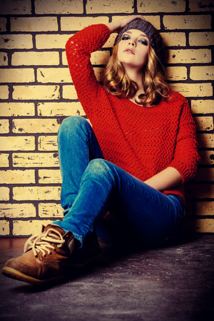 Modern girl teenager sitting relaxed by a brick wall. Teen generation. Youth fashion style.の写真素材