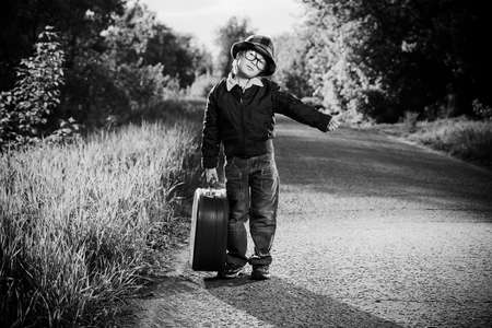 Portrait of a cute dreamy boy standing with his old suitcase outdoor. Summer day. Adventure.の写真素材