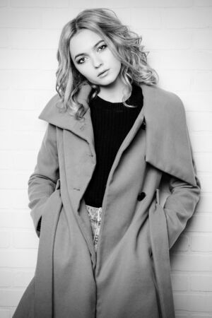 Young fashion woman. Black-and-white portrait of a beautiful blonde girl posing in studio in a coat. Beauty, fashion.の写真素材