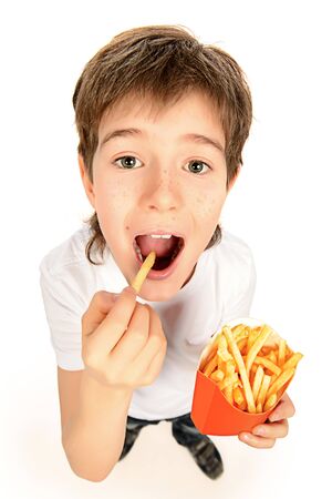 Happy nine year old boy eating french fries and laughing. Fast food. Concept of healthy and unhealthy food. Isolated over white.の写真素材