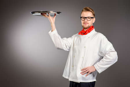Portrait of a male chef cook in uniform holding empty tray. Copy space. Occupation. Studio shot.の写真素材