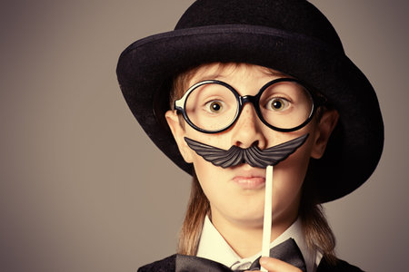 Funny boy in a bowler hat and spectacles plays with false mustache. Generation concept. Children...