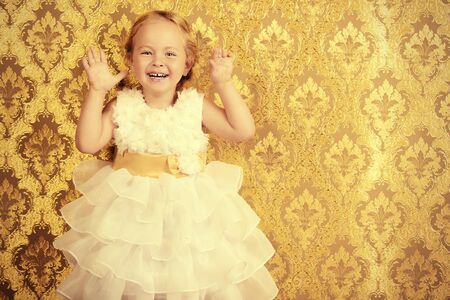 Happy little girl in a beautiful white dress standing by the vintage wall. Childhood. Holiday, birthday.の写真素材