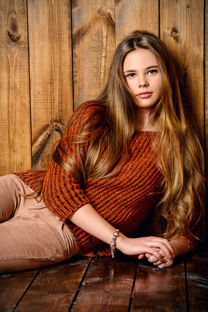 Pretty teenager girl in casual clothes sitting by a wooden wall. Modern teen generation. Youth fashion. Healthy hair, haircare.の写真素材