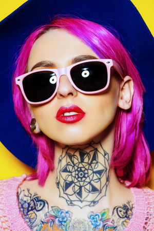 Pretty girl with crimson hair wearing bright clothes and sunglasses posing over yellow background. Bright style, fashion. Optics style. Tattoo.の写真素材
